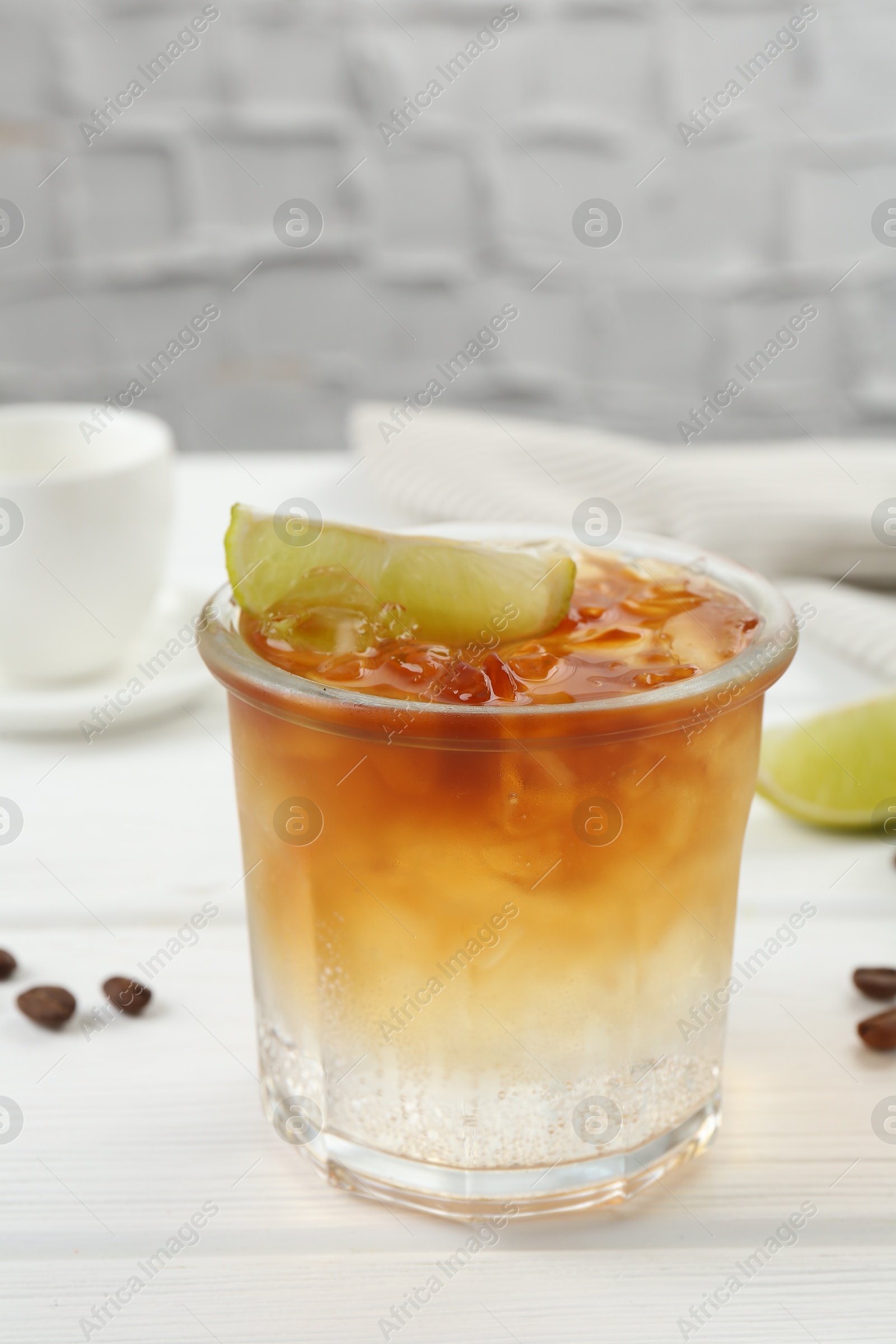 Photo of Refreshing espresso tonic drink with slice of lime and coffee beans on white wooden table, closeup