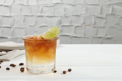 Photo of Refreshing espresso tonic drink with slice of lime and coffee beans on white wooden table, space for text