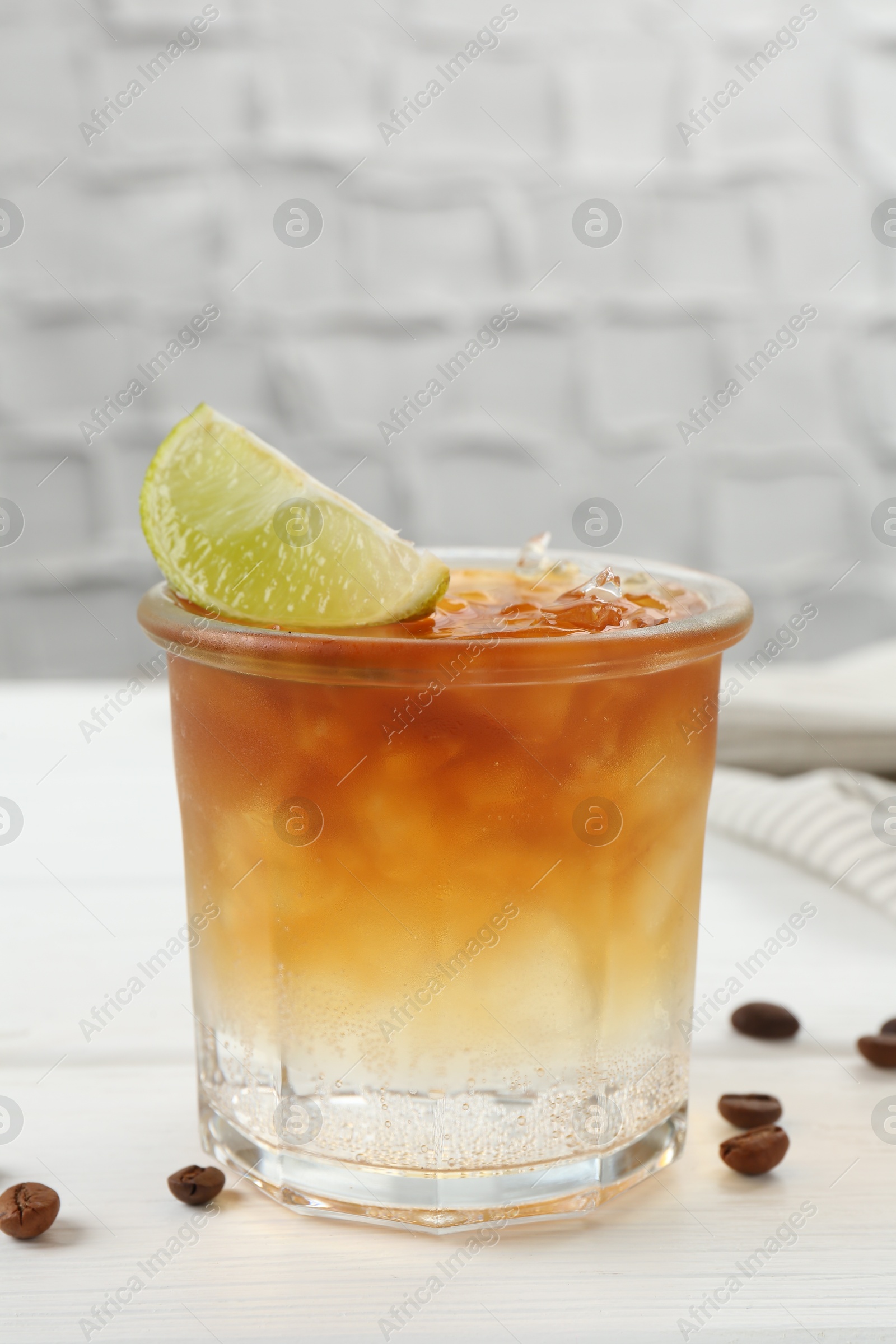 Photo of Refreshing espresso tonic drink with slice of lime and coffee beans on white wooden table, closeup