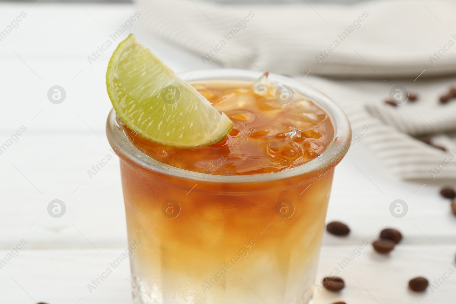 Photo of Refreshing espresso tonic drink with slice of lime and coffee beans on white wooden table, closeup