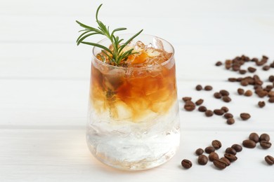 Refreshing espresso tonic drink with rosemary and coffee beans on white wooden table, closeup