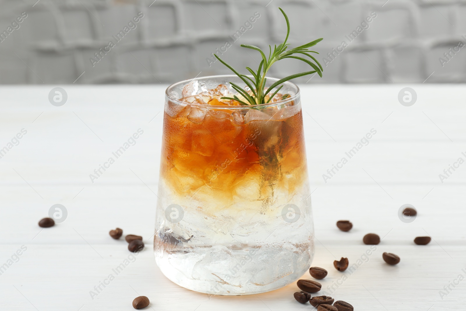 Photo of Refreshing espresso tonic drink with rosemary and coffee beans on white wooden table, closeup