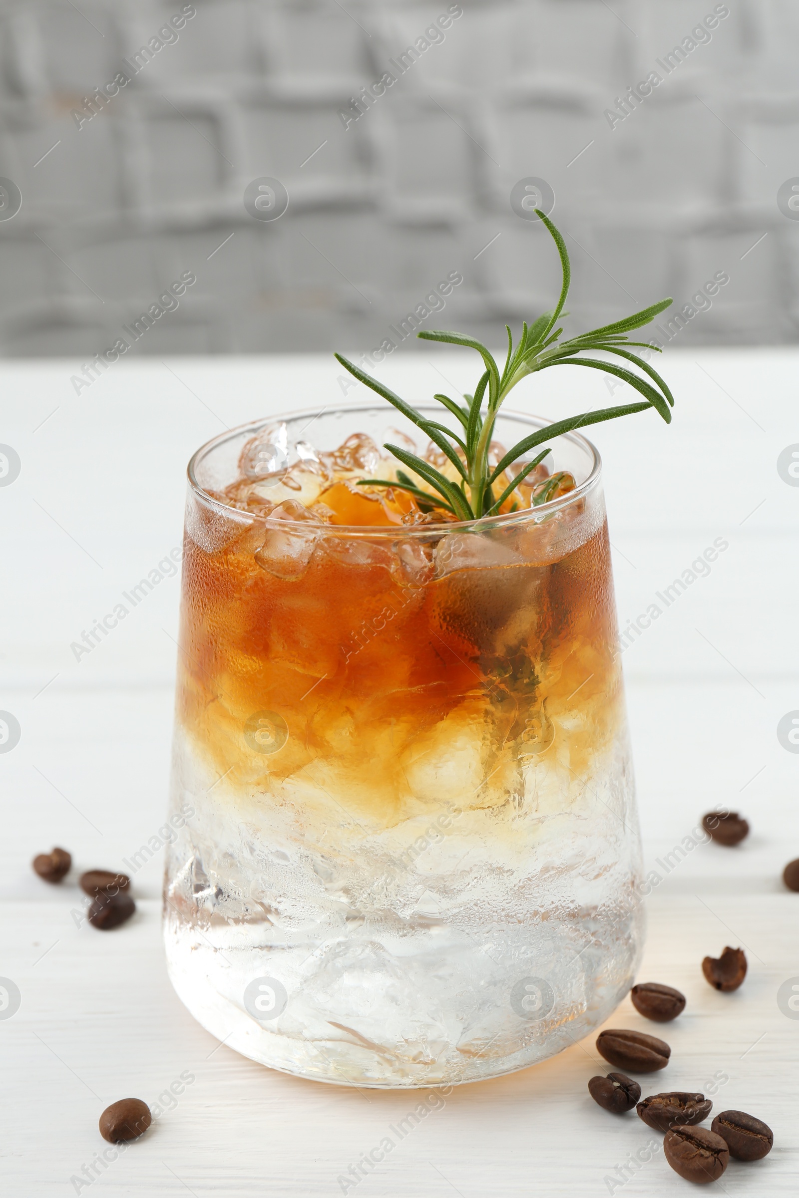 Photo of Refreshing espresso tonic drink with rosemary and coffee beans on white wooden table, closeup