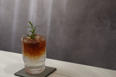 Refreshing espresso tonic drink with rosemary on white wooden table, space for text