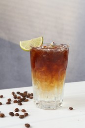 Photo of Refreshing espresso tonic drink with slice of lime and coffee beans on white wooden table