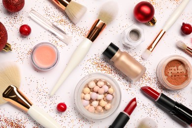 Different makeup brushes, decorative cosmetics and Christmas decor on white background, flat lay