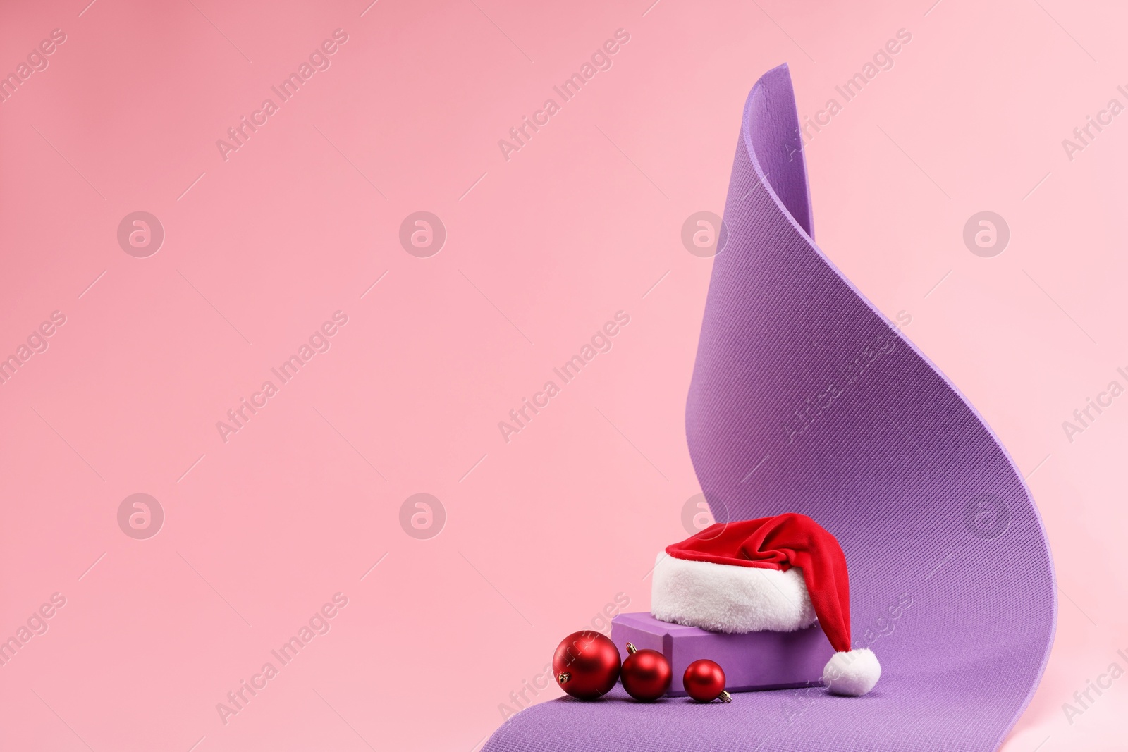 Photo of Yoga mat, Santa hat and baubles on pink background, space for text