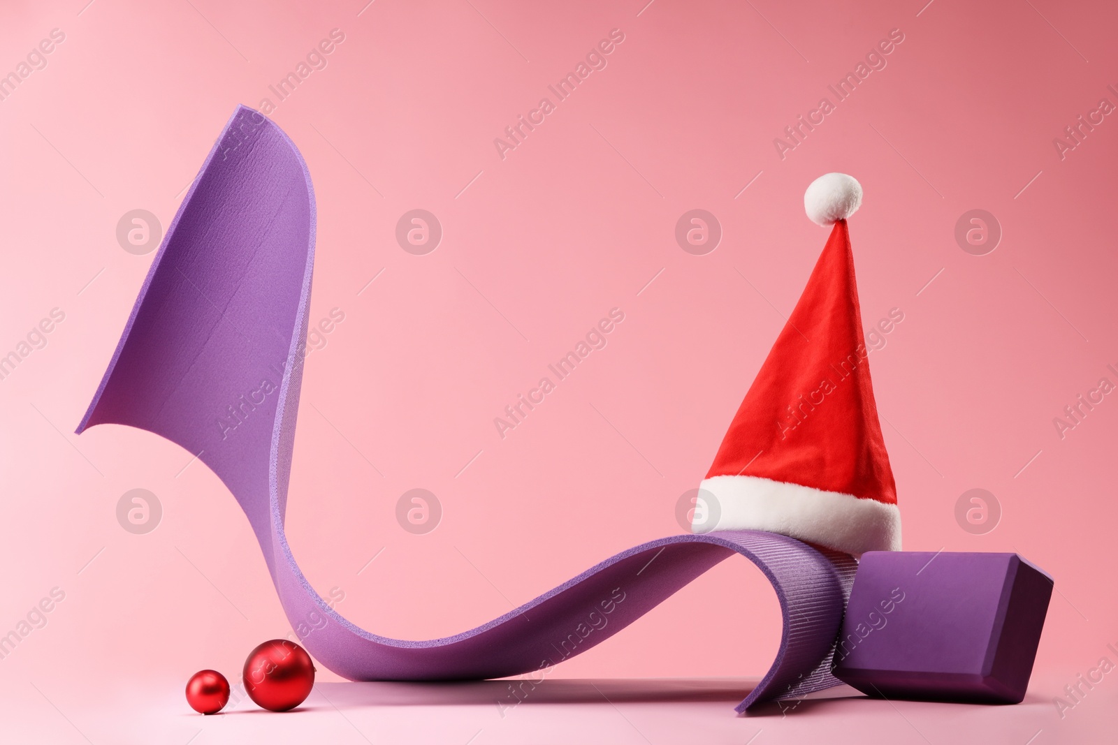 Photo of Yoga mat, block, Santa hat and baubles on pink background