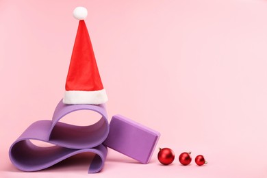 Photo of Yoga mat, Santa hat and baubles on pink background, space for text