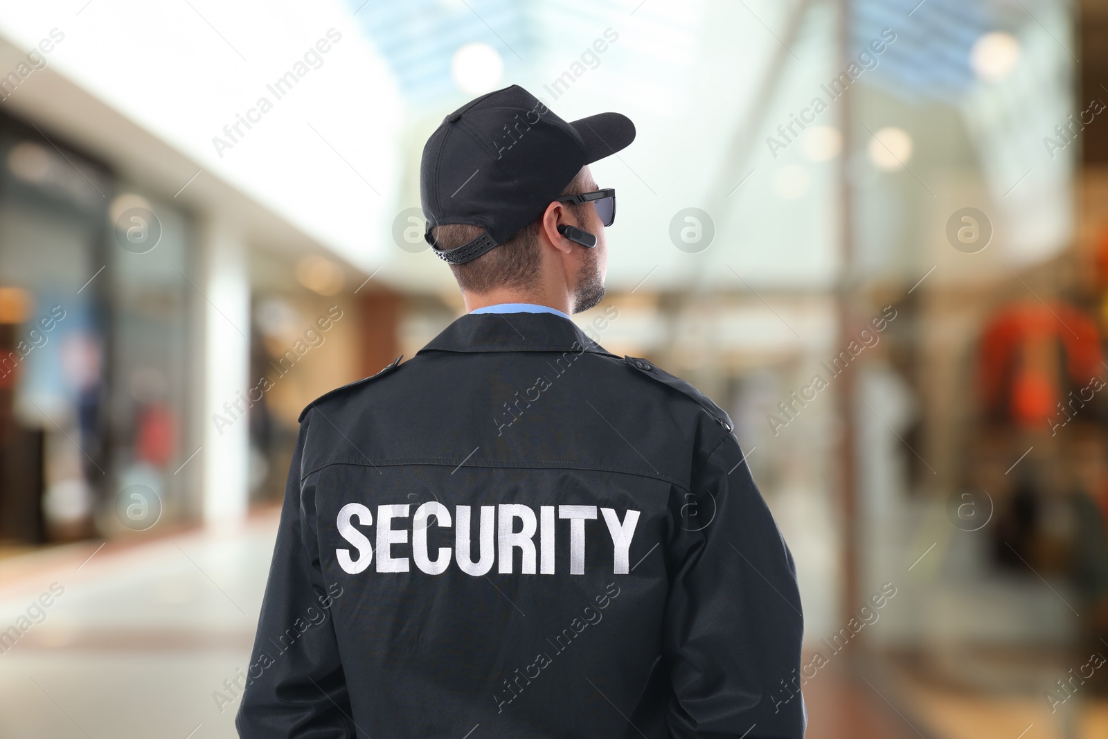 Image of Security guard in uniform and earpiece in shopping mall, back view