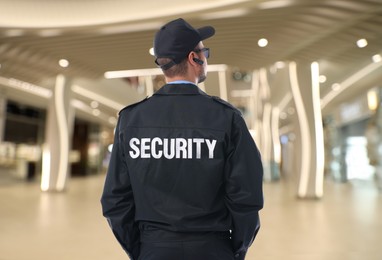 Security guard in uniform and earpiece in shopping mall, back view