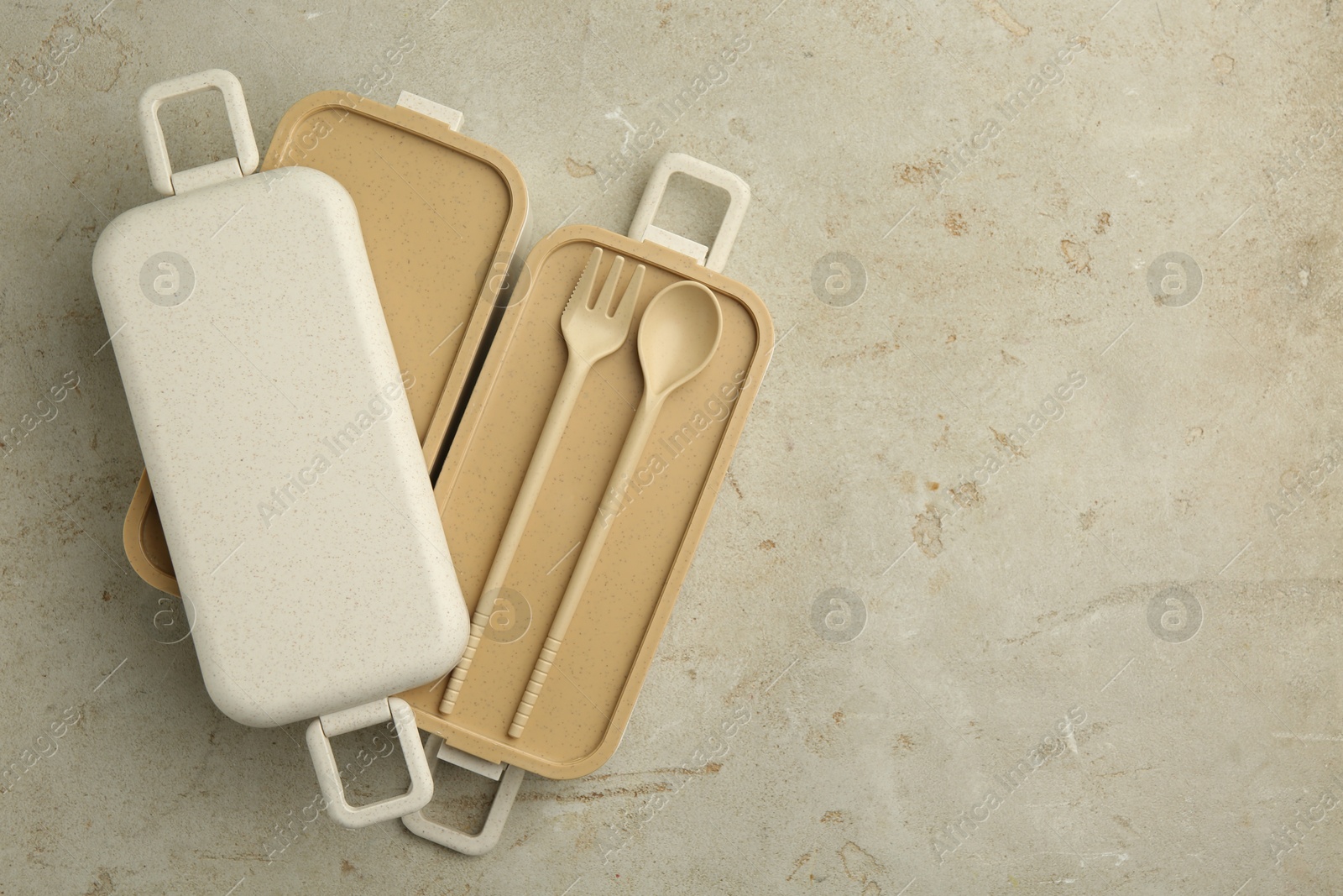 Photo of Compartments of plastic lunch box with cutlery on grey table, top view. Space for text