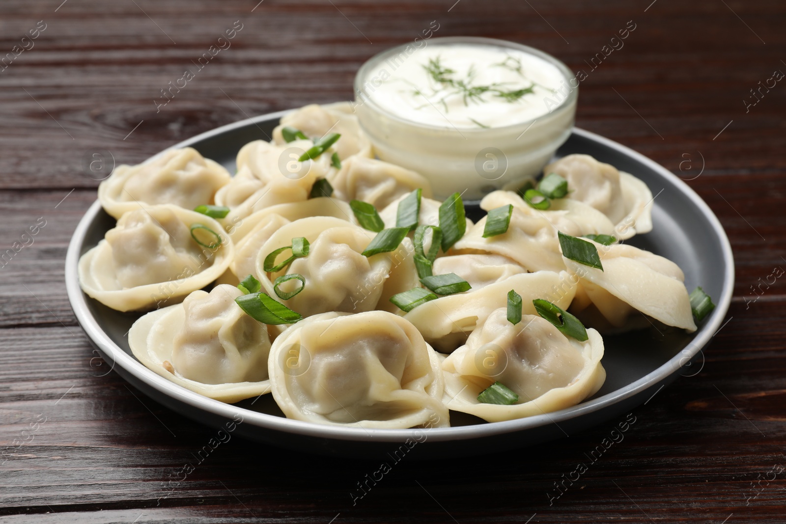 Photo of Delicious pelmeni with green onion served on wooden table, closeup