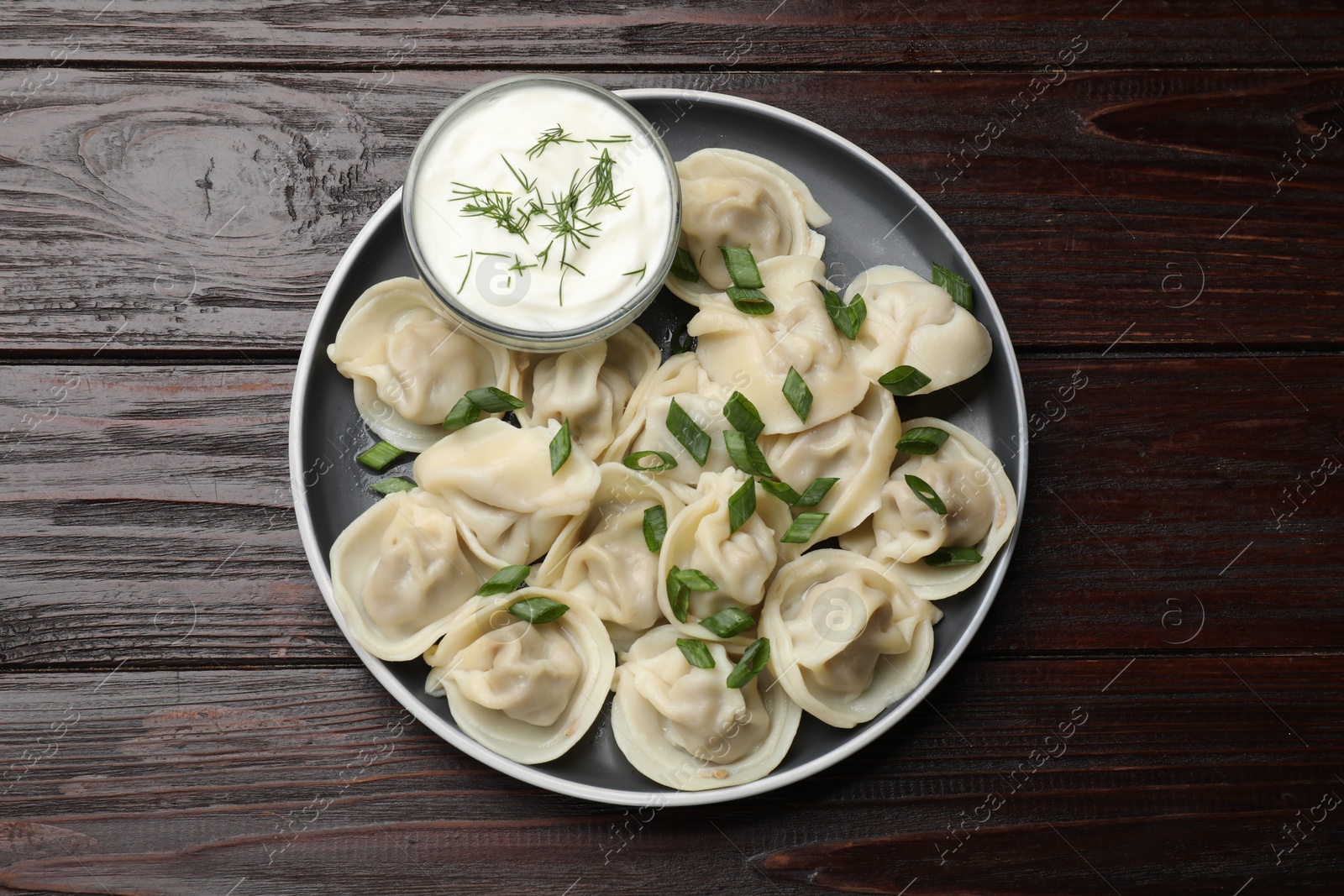 Photo of Delicious pelmeni with green onion served on wooden table, top view