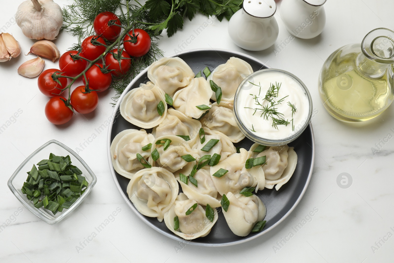 Photo of Delicious pelmeni with green onion served on white marble table, flat lay