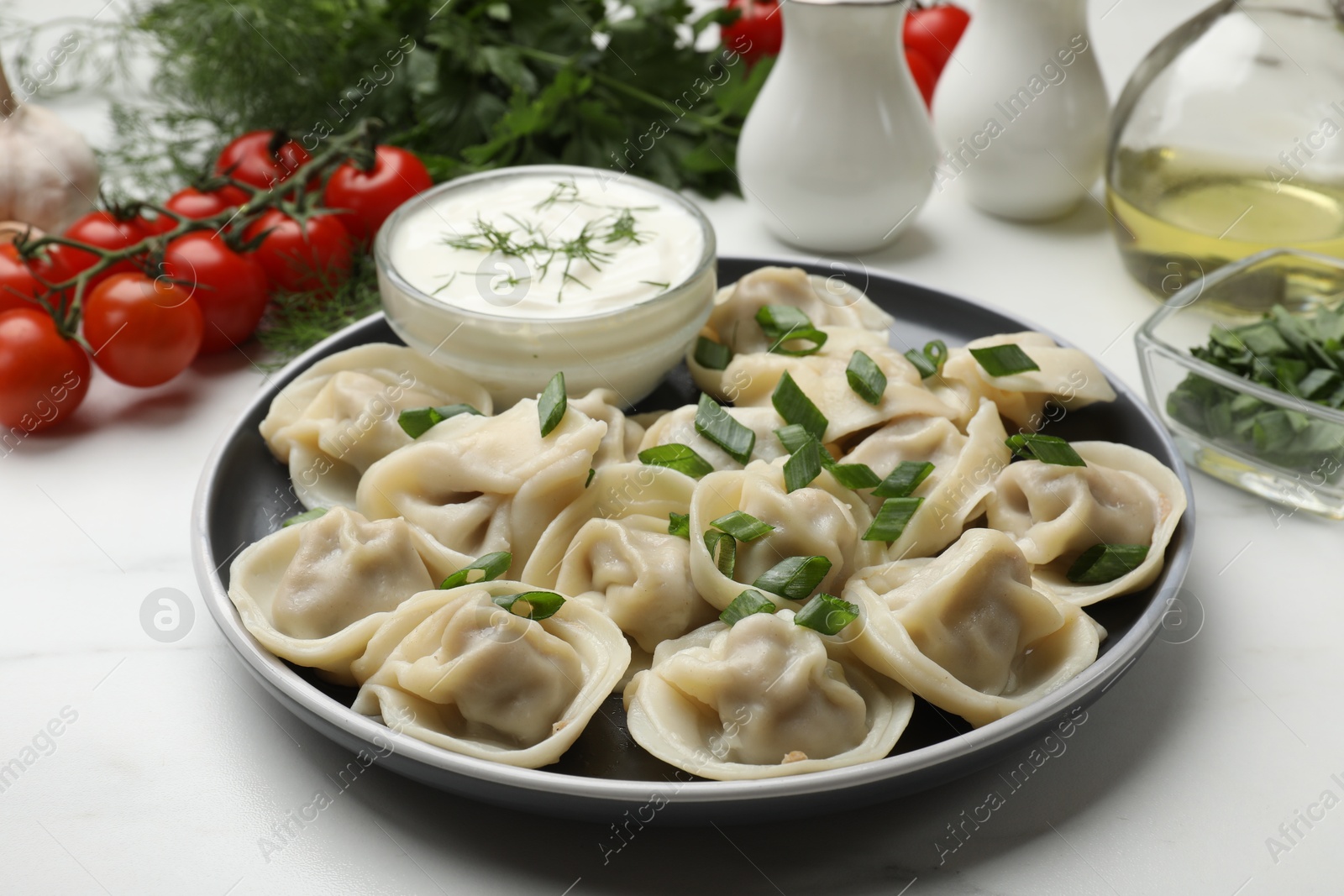 Photo of Delicious pelmeni with green onion served on white marble table, closeup