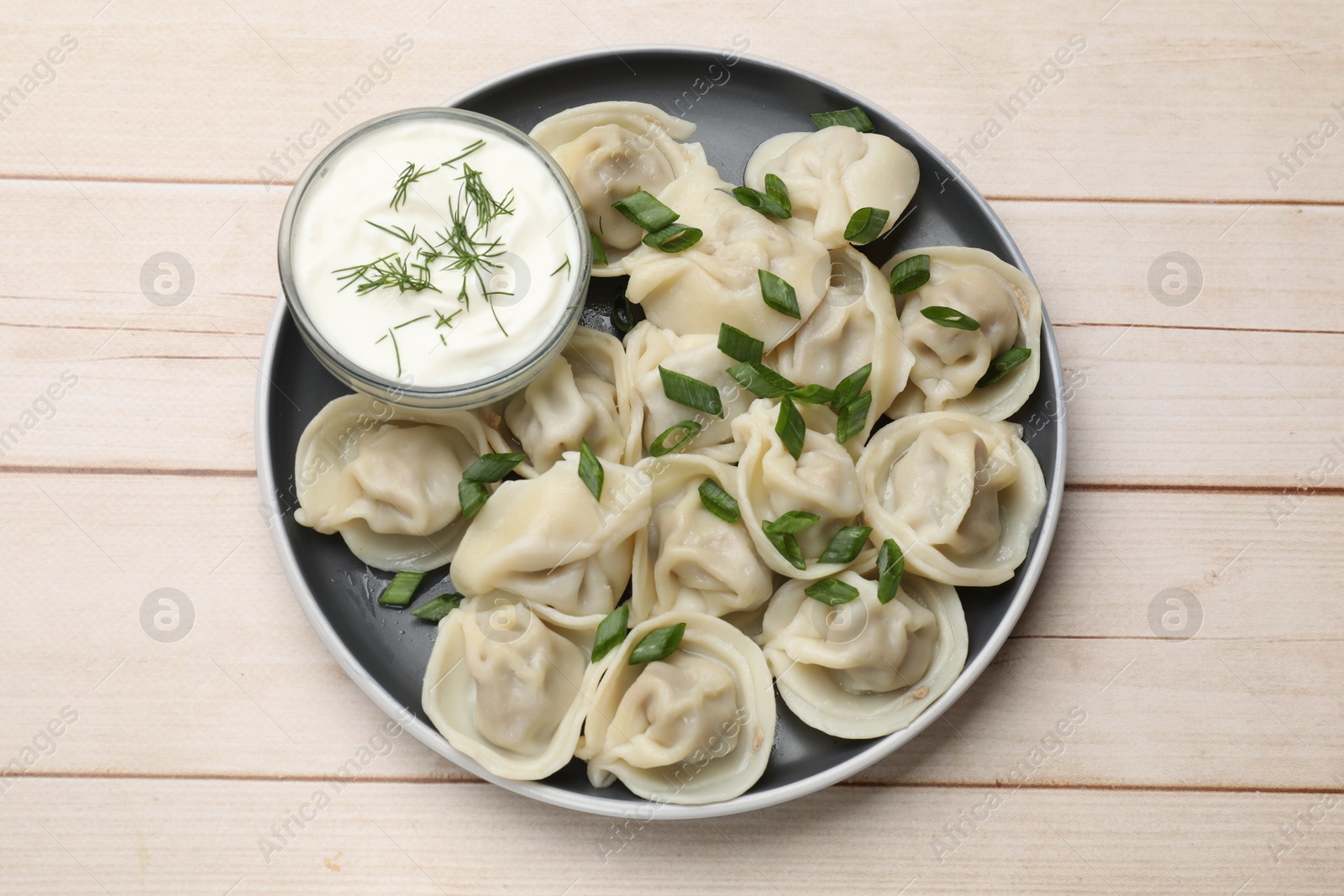 Photo of Delicious pelmeni with green onion served on wooden table, top view