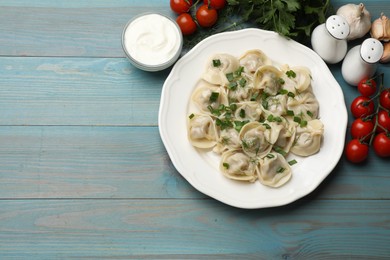 Photo of Delicious pelmeni with green onion served on blue wooden table, flat lay. Space for text