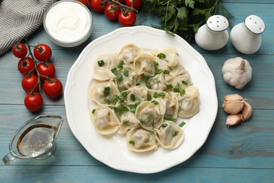 Photo of Delicious pelmeni with green onion served on blue wooden table, flat lay