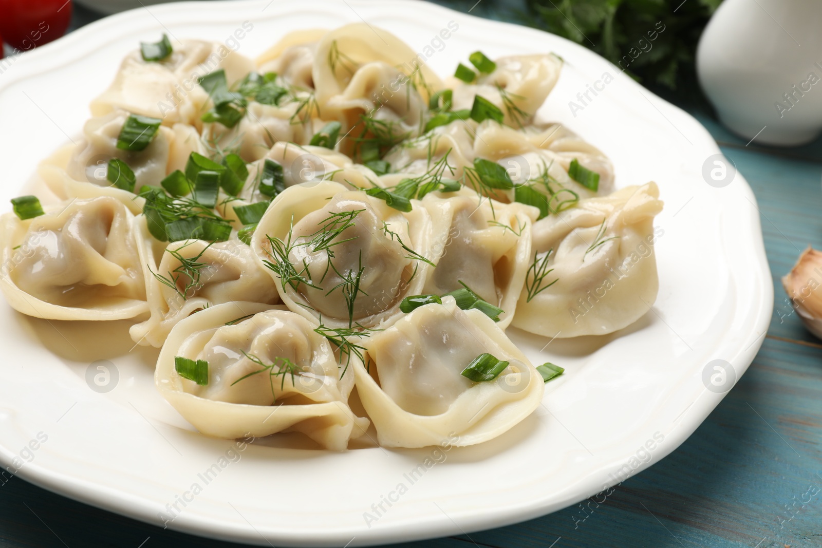 Photo of Delicious pelmeni with green onion and dill on blue table, closeup