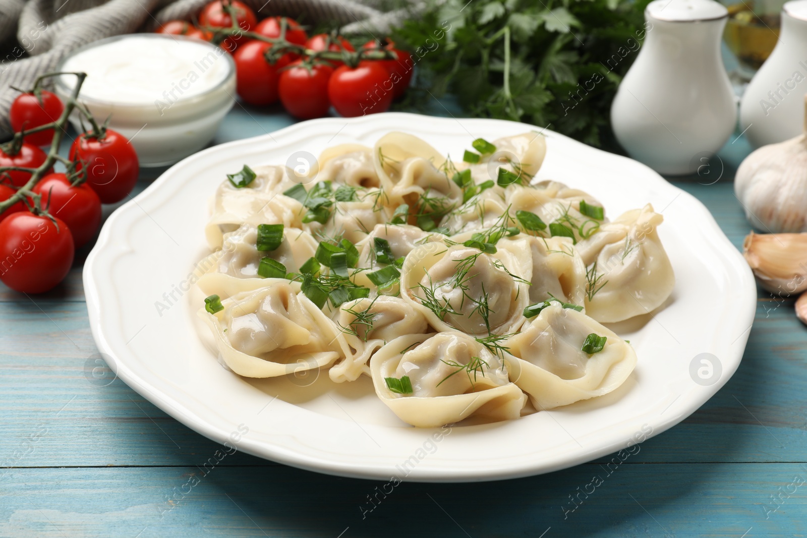 Photo of Delicious pelmeni with green onion served on blue wooden table