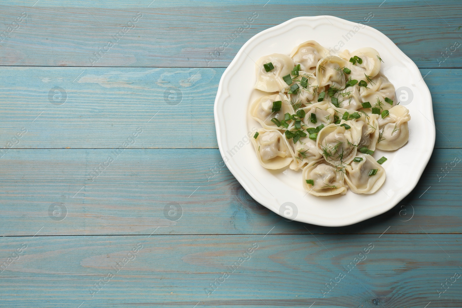 Photo of Delicious pelmeni with green onion and dill on blue wooden table, top view. Space for text