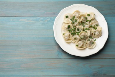 Photo of Delicious pelmeni with green onion and dill on blue wooden table, top view. Space for text