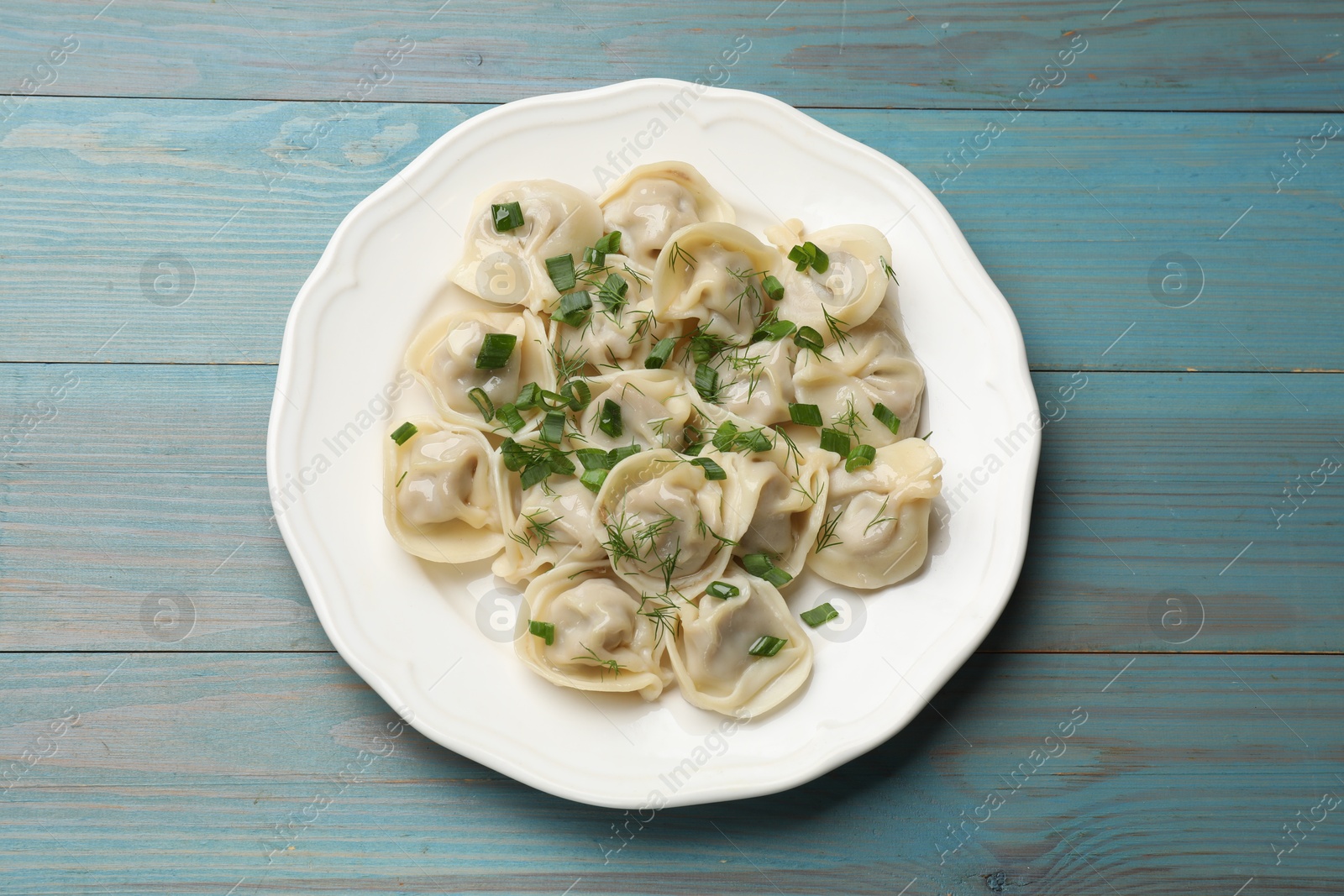 Photo of Delicious pelmeni with green onion and dill on blue wooden table, top view