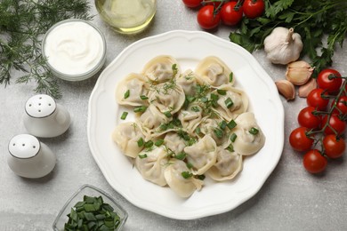 Delicious pelmeni with green onion served on grey textured table, flat lay