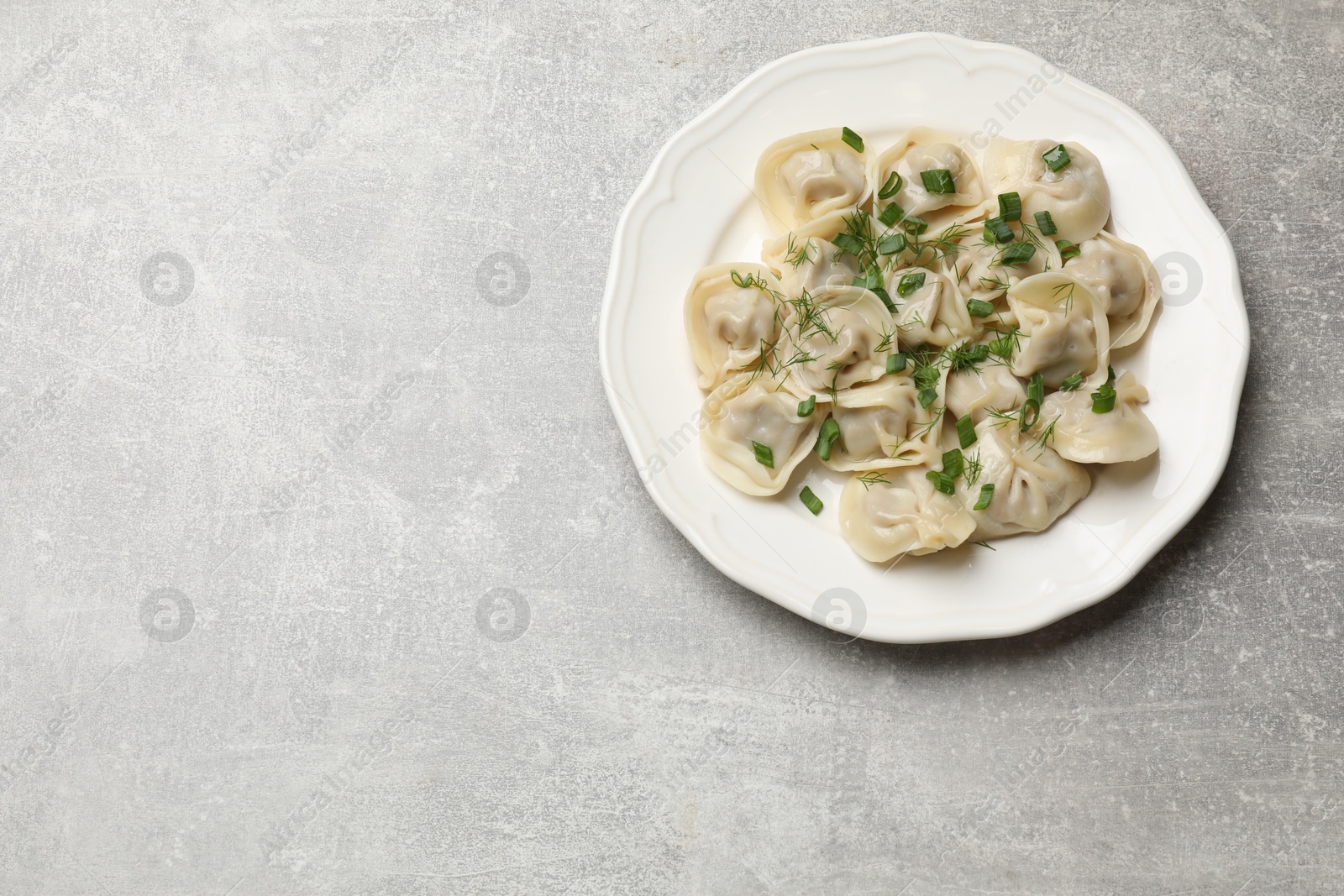 Photo of Delicious pelmeni with green onion and dill on grey textured table, top view. Space for text