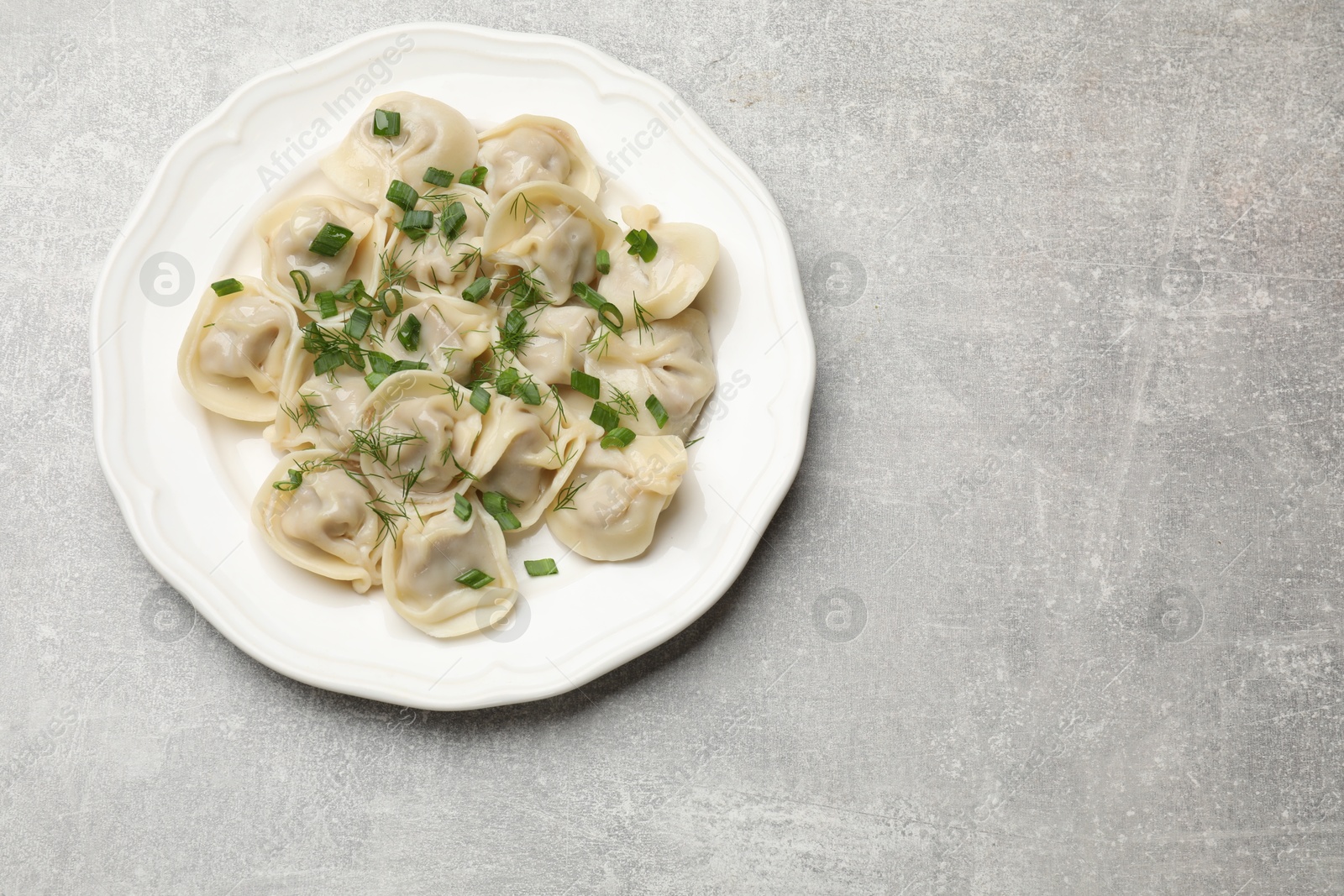 Photo of Delicious pelmeni with green onion and dill on grey textured table, top view. Space for text