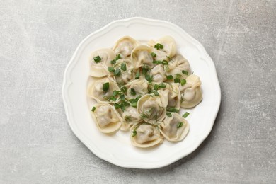 Photo of Delicious pelmeni with green onion and dill on grey textured table, top view