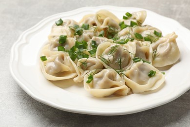 Photo of Delicious pelmeni with green onion and dill on grey textured table, closeup