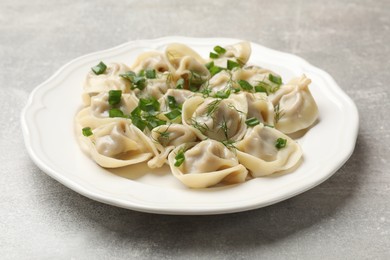 Photo of Delicious pelmeni with green onion and dill on grey textured table, closeup