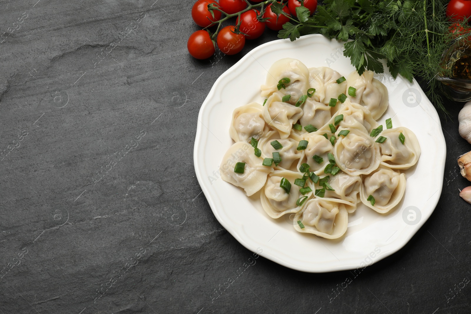 Photo of Delicious pelmeni with green onion served on grey textured table, flat lay. Space for text