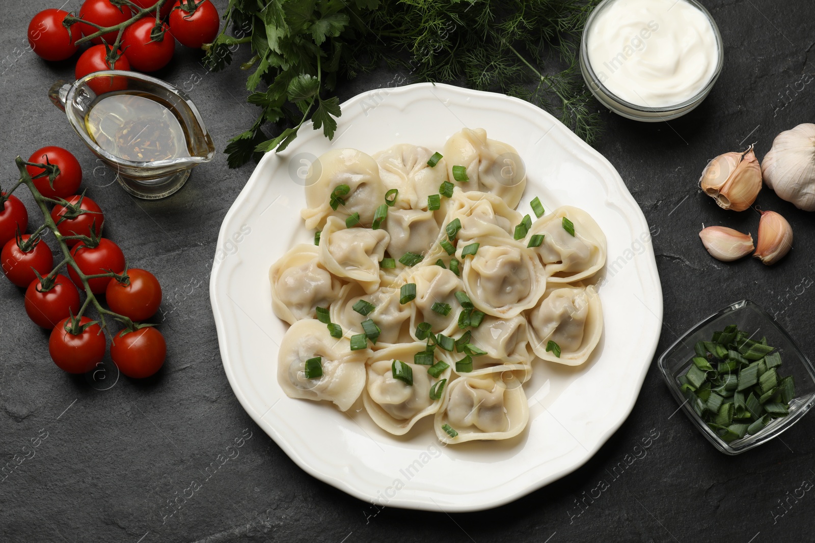 Photo of Delicious pelmeni with green onion served on grey textured table, flat lay