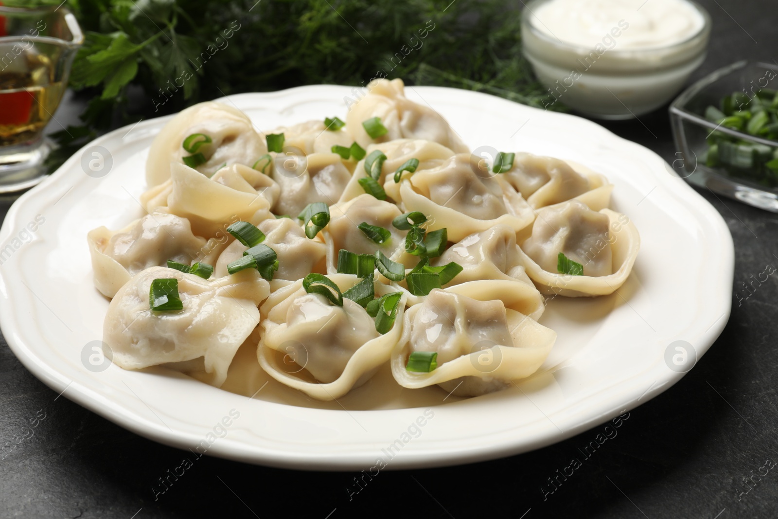 Photo of Delicious pelmeni with green onion on grey textured table, closeup