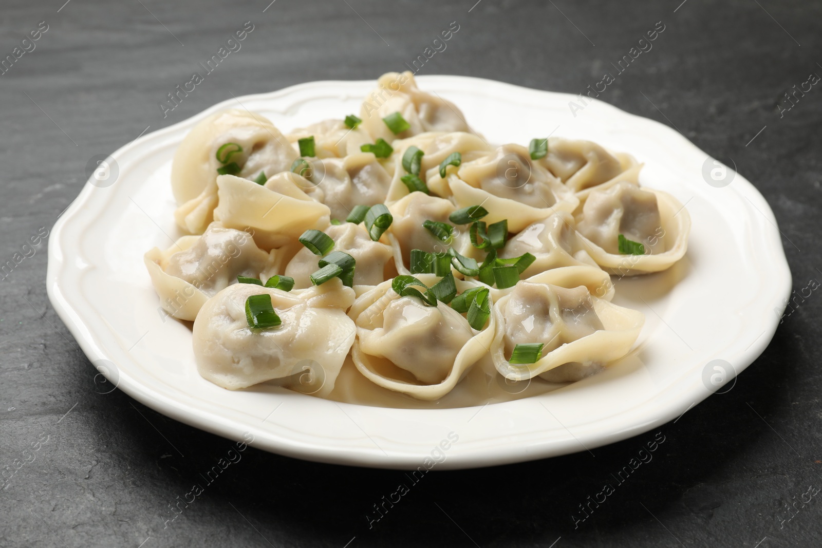 Photo of Delicious pelmeni with green onion on grey textured table, closeup