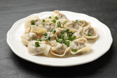 Photo of Delicious pelmeni with green onion on grey textured table, closeup