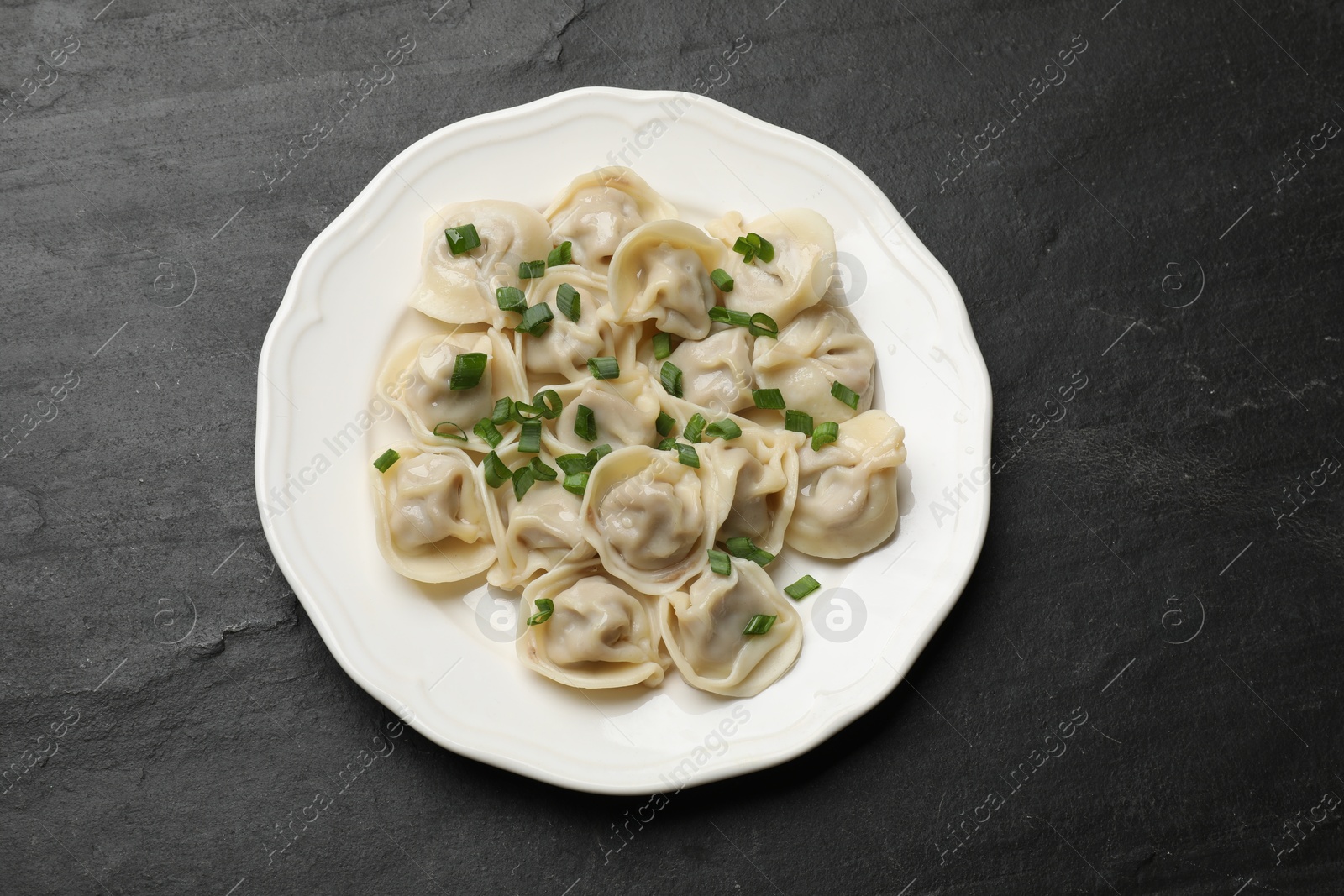 Photo of Delicious pelmeni with green onion on grey textured table, top view