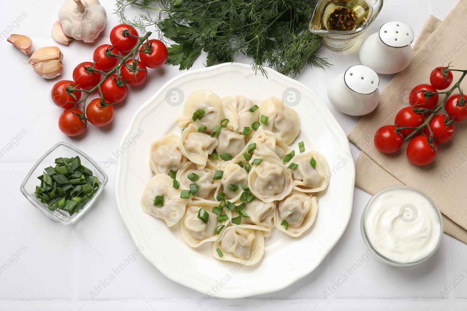 Photo of Delicious pelmeni with green onion served on white tiled table, flat lay