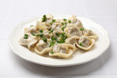 Delicious pelmeni with green onion on white tiled table, closeup