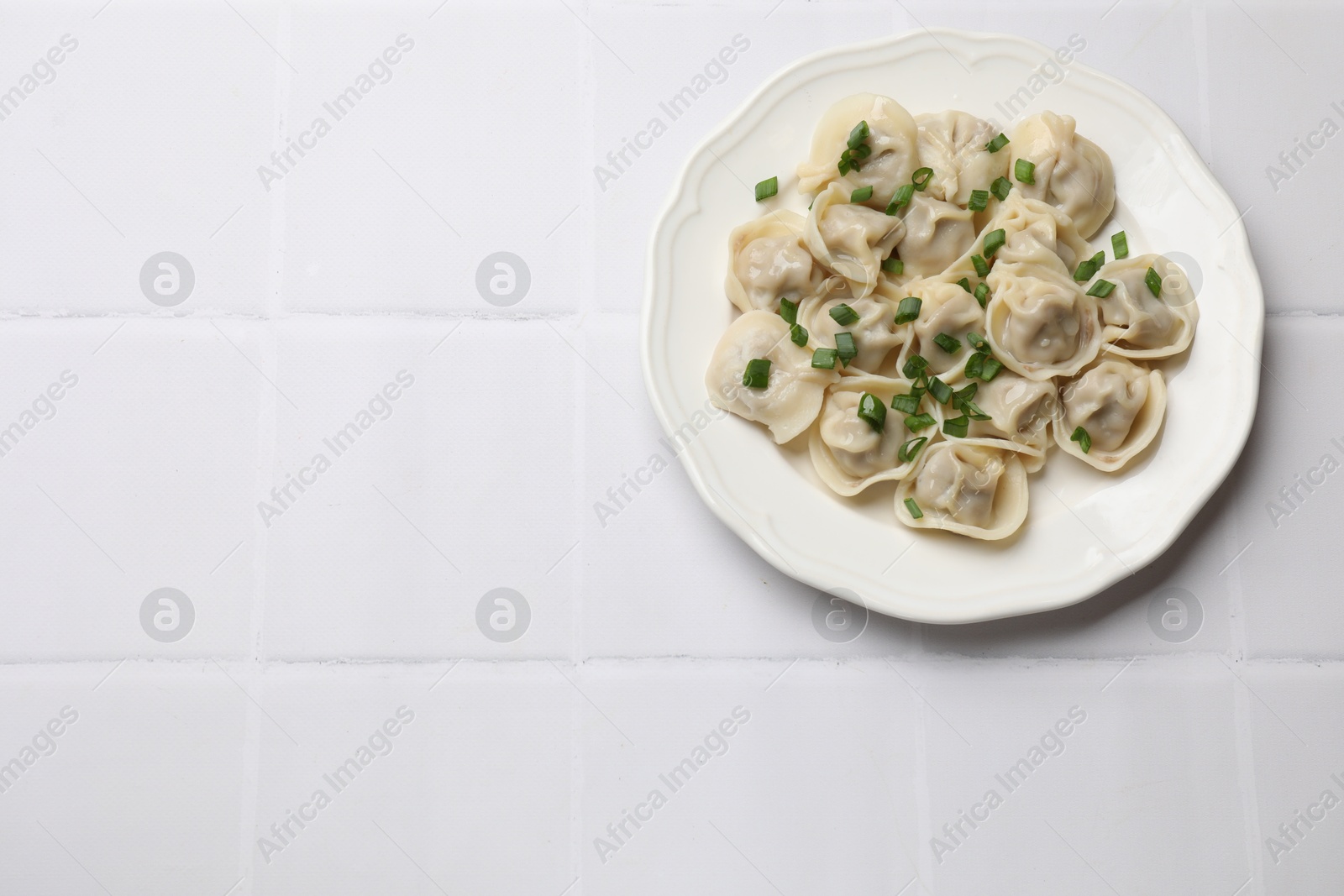 Photo of Delicious pelmeni with green onion on white tiled table, top view. Space for text