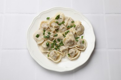 Photo of Delicious pelmeni with green onion on white tiled table, top view