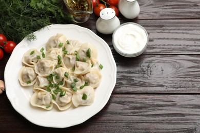 Photo of Delicious pelmeni with green onion served on wooden table, flat lay. Space for text