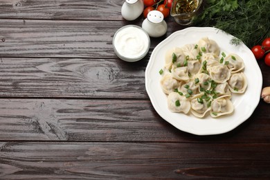 Photo of Delicious pelmeni with green onion served on wooden table, flat lay. Space for text