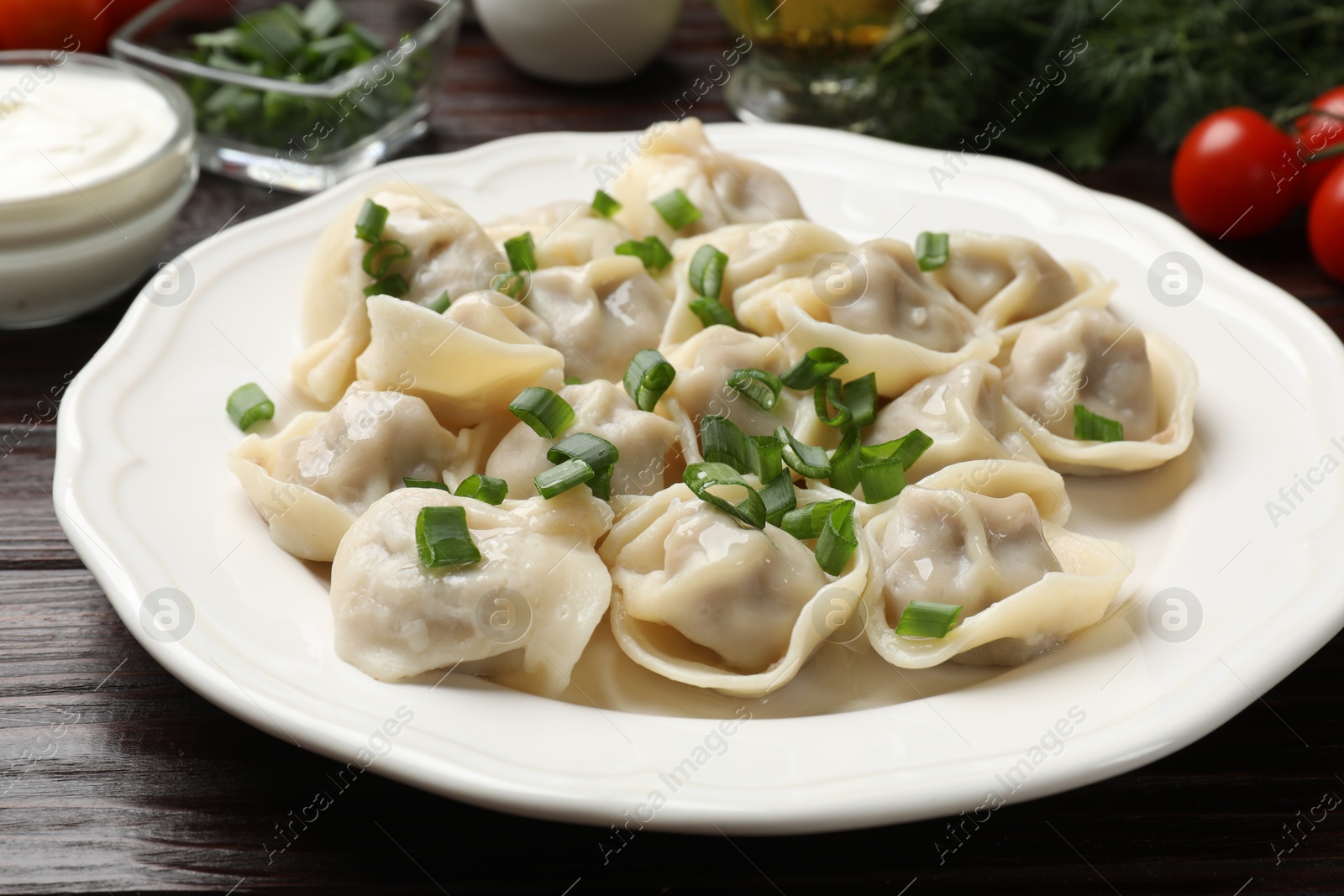 Photo of Delicious pelmeni with green onion on wooden table, closeup