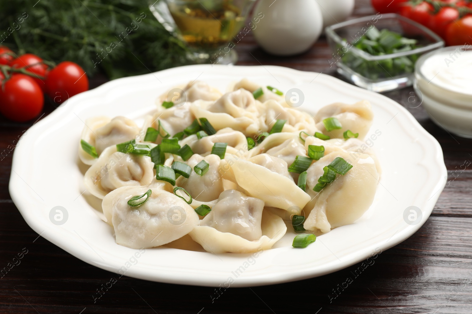 Photo of Delicious pelmeni with green onion on wooden table, closeup