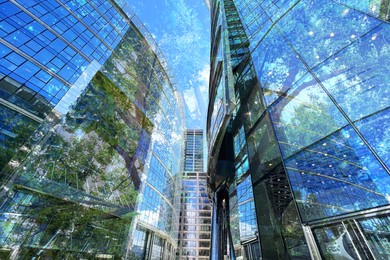 Image of Environment preservation. Double exposure of modern buildings and trees against blue sky, low angle view