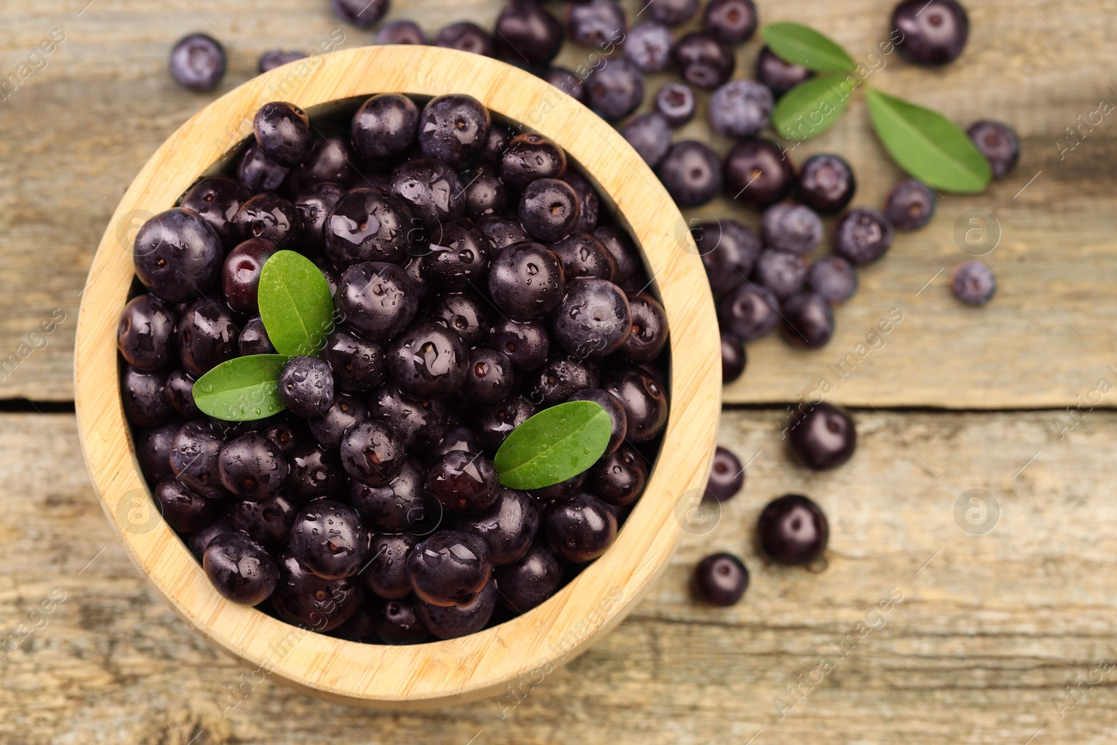 Photo of Ripe acai berries and leaves in bowl on wooden table, top view